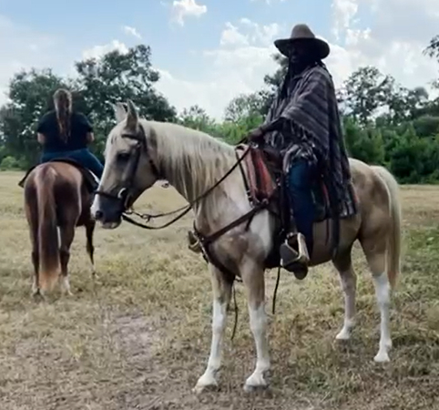 Two people on horses in a field with trees, one in a poncho and hat.