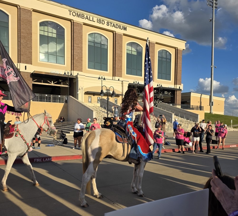 Person on horse holding US flag in front of stadium with crowd.