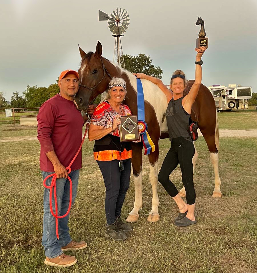 Three people with a horse holding awards, a windmill in the background.