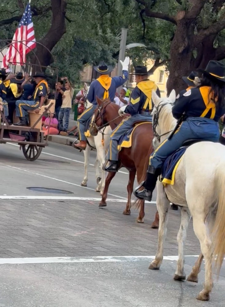 Parade with people in uniform on horses and a wagon with an American flag.