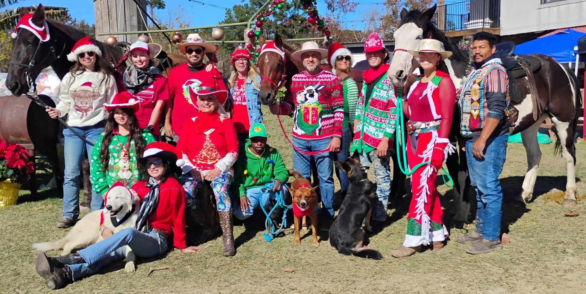 Group of people in festive attire with horses and dogs, outdoors on a sunny day.