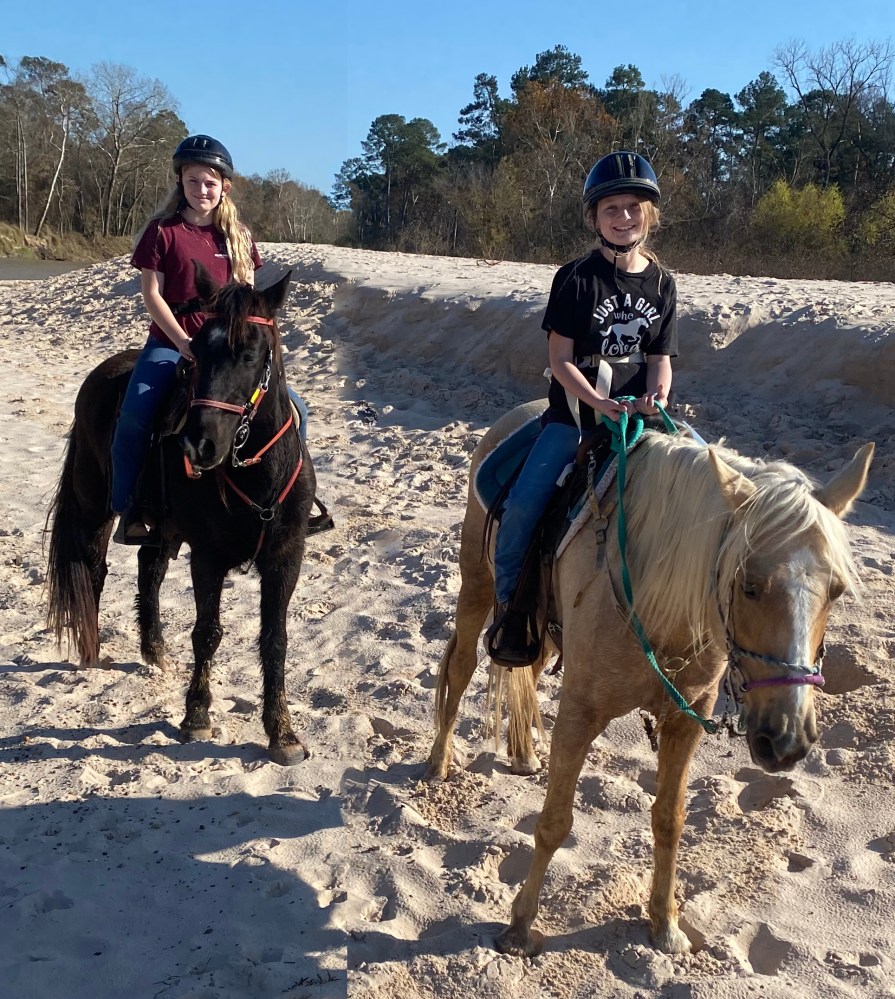 Two people riding horses on a sandy path, wearing helmets.