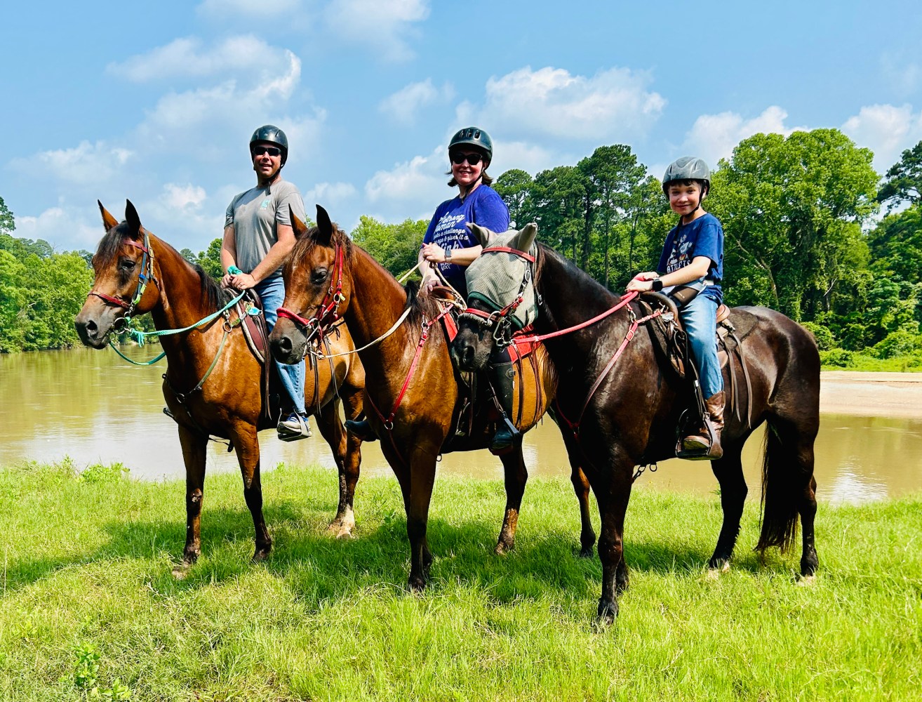 Three people on horses near a lake under a blue sky.