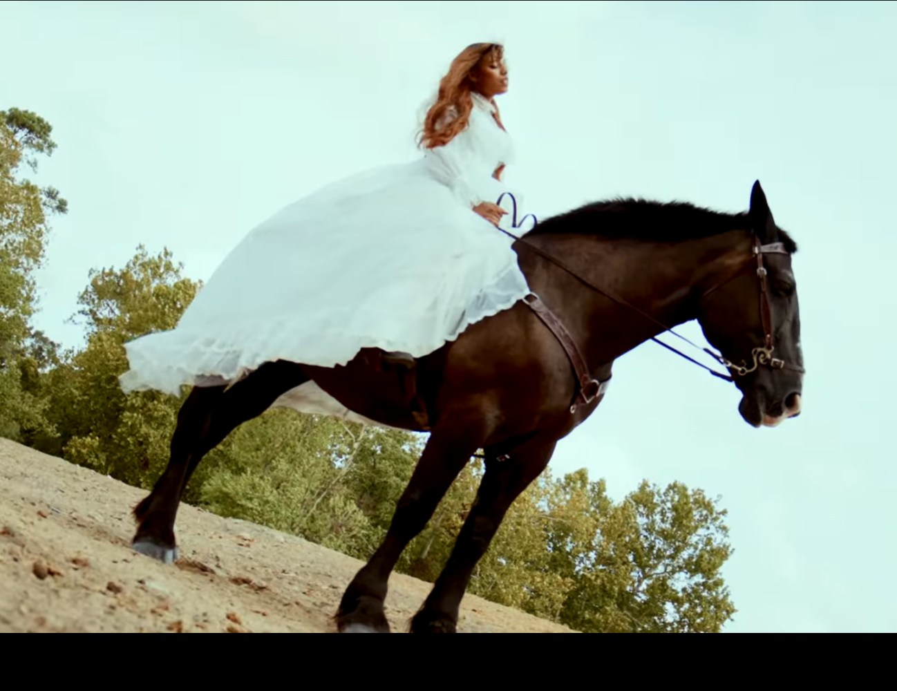 Woman in white dress riding a black horse outdoors.