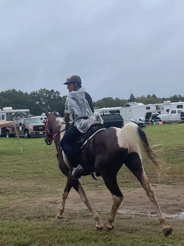 Person in raincoat riding a horse at a campsite.